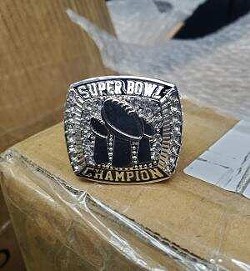 A silver ring reads "Super Bowl Champion" with images of three Lombardi trophies.