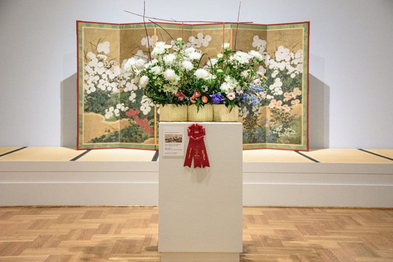 A green-based flower display in front of a piece of artwork.