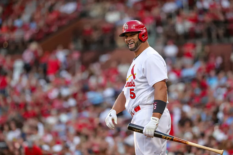 Albert Pujols smiles in a Cardinals uniform with a bat in his hand.