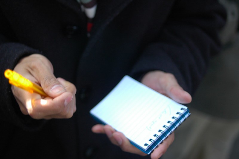A close up of a man taking notes on a journalist-style notepad.
