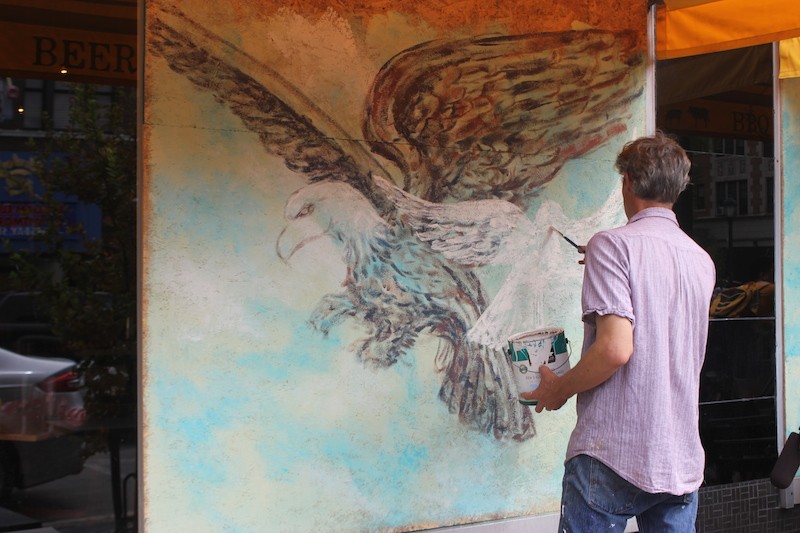 An artist paints the plywood covering Salt + Smoke with an illustration showing an eagle — and a dove. - PHOTO BY SARAH FENSKE